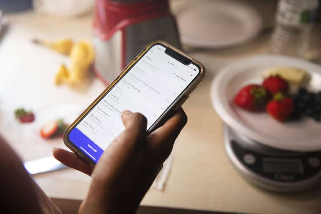 Person using MyFitnessPal app on phone to track lunch meal with fresh strawberries nearby